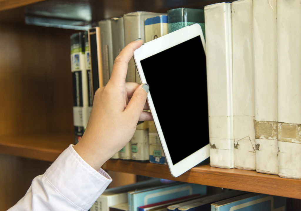 Closeup hand putting a tablet pc in the shelves in the library