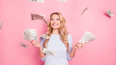 Młoda kobieta stoi na różowym tle i trzyma banknoty do oszczędzania